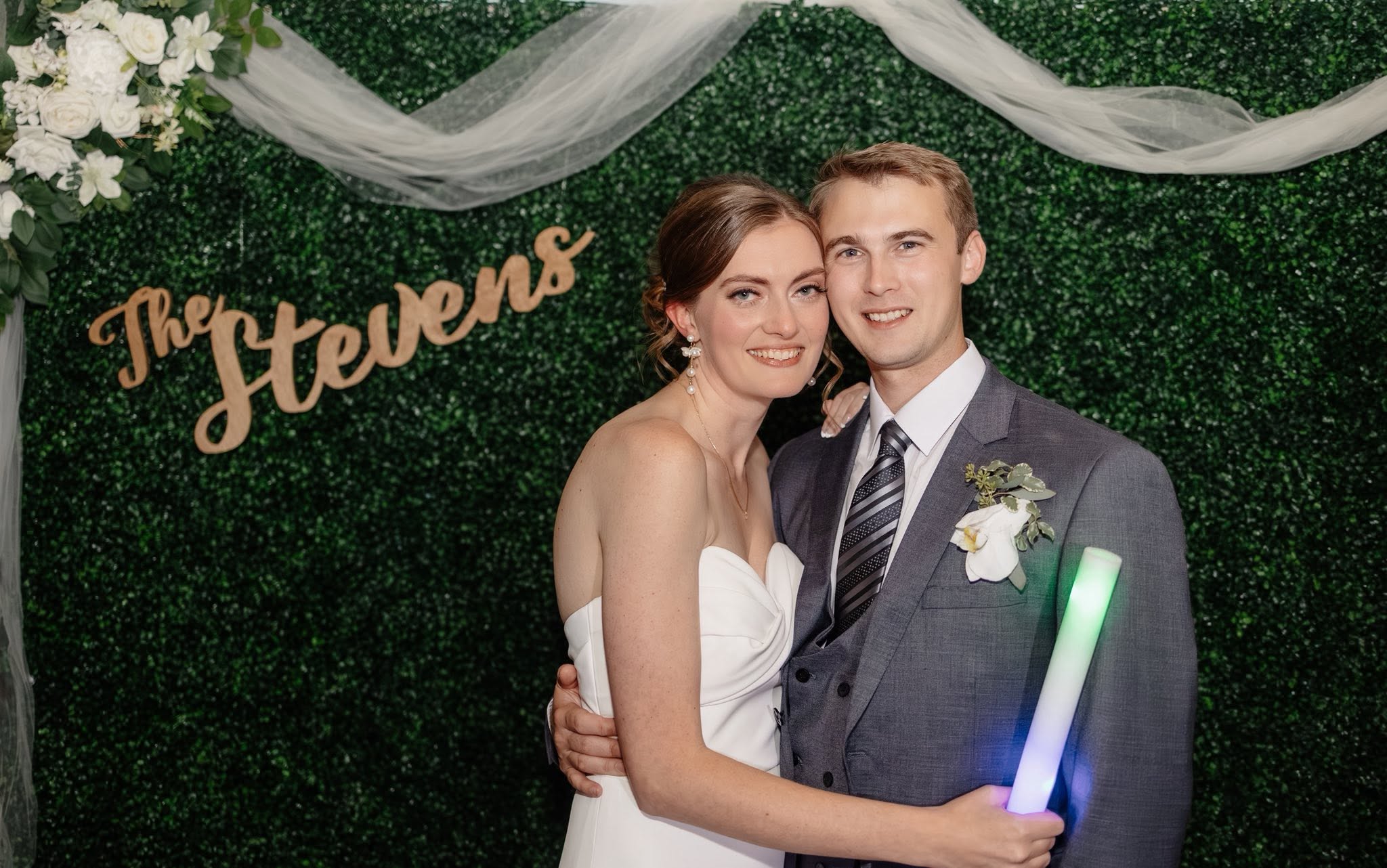 Couple portrait in front of greenery backdrop wall with custom name sign — Stevens Wedding